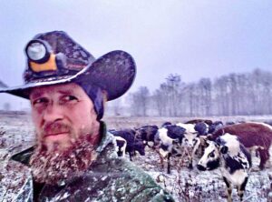 Will McGee with a cowboy hat in a field with cows